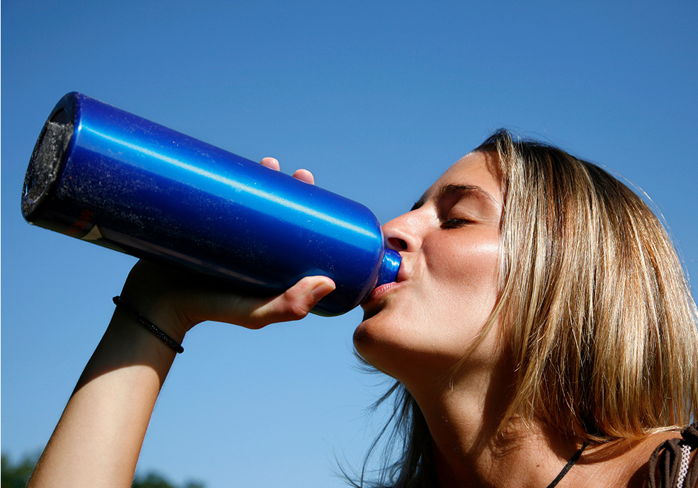 image femme qui boit dans sa gourde en extérieur