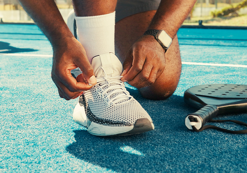 homme qui refait ses lacets de ses chaussure de padel sur un terrain de padel