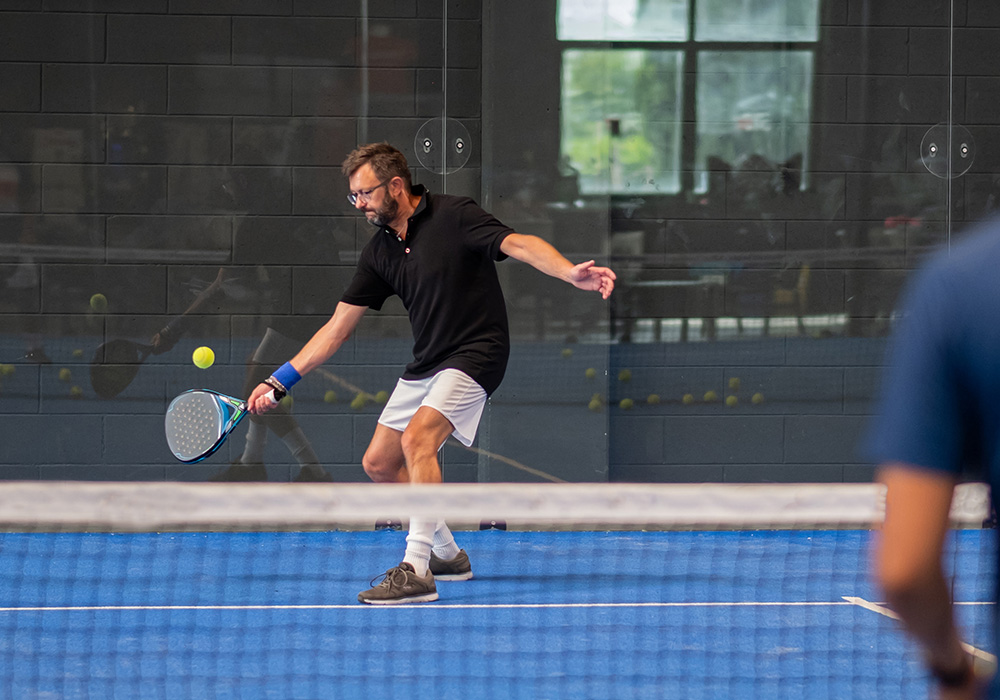joueur homme en tenue légère de padel qui renvoie une balle