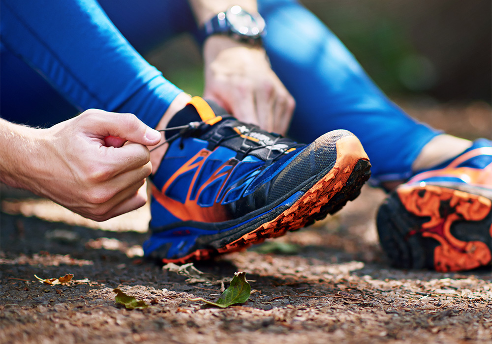 homme qui refait ses lacets de ses chaussures de trail bleu orange a crampons